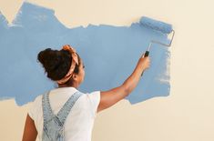 a woman in overalls painting a wall with blue paint