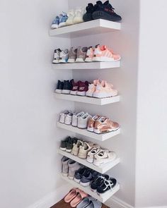 a white shelf with several pairs of shoes on it in the corner of a room