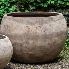 two large cement pots sitting next to each other on top of gravel covered ground with trees in the background