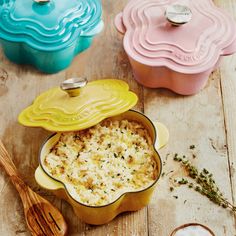 three different colored casserole dishes and spoons on a wooden table with utensils