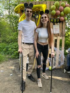 a man and woman standing next to each other holding crutches in front of balloons