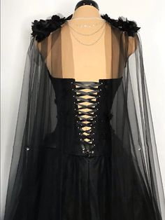 a black dress with sheer sleeves and laces on the neckline is displayed in front of a mannequin