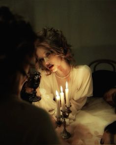 a woman sitting at a table with candles in front of her and other people around her