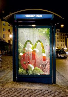 a bus stop with an advertisement on the side of it's glass window at night