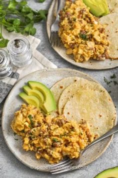 two plates filled with eggs and avocado on top of a table next to silverware