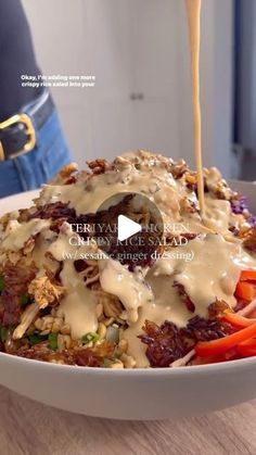 a person pouring sauce on a bowl of food with carrots and celery