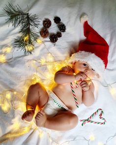 a baby wearing a santa hat laying on top of a bed next to christmas lights