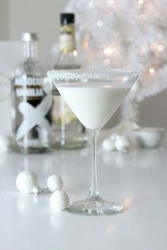 two martini glasses filled with white liquid on a table next to bottles and christmas decorations