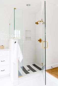 a white bathroom with black and white flooring, gold fixtures and glass shower doors