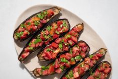 an oval plate topped with sliced eggplant covered in tomatoes and garnish