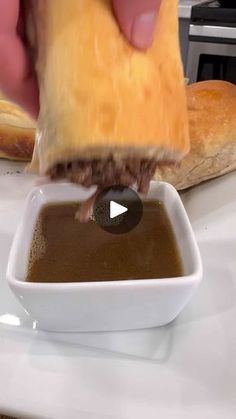 a person dipping something into a bowl of brown sauce on top of a white plate