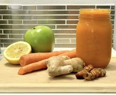 carrots, lemon and ginger sit on a cutting board next to an apple in a mason jar