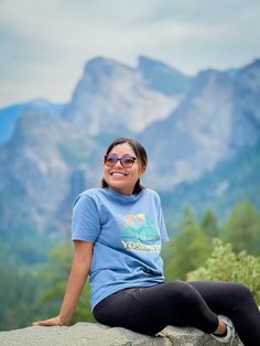 a woman sitting on top of a rock with mountains in the background