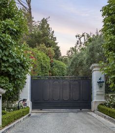 an entrance to a home with trees and bushes around it, leading into the driveway