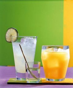 two glasses filled with drinks sitting on top of a purple and green table cloth next to each other