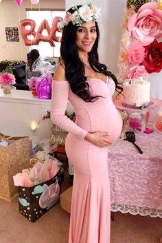 a pregnant woman in a pink dress standing next to a table