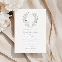 the wedding card is laying on top of some white flowers and cloth with an elegant monogrammed design