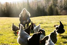 a woman kneeling down next to chickens on a lush green field with trees in the background