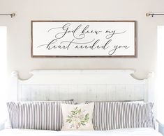 a white bed topped with pillows next to a wooden sign that says easy let's get