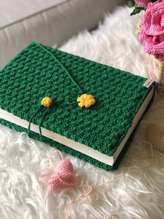 a green crocheted book with yellow flowers on it next to a pink flower pot