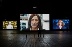 a person standing in front of three large screens with faces on them at the same time