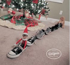 an elf is sitting on the floor next to some sneakers and a christmas tree with presents