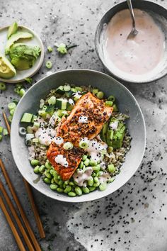 a bowl filled with rice, peas and salmon next to chopsticks on the side