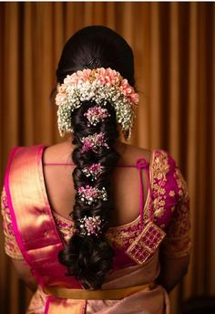 a woman with flowers in her hair wearing a pink and gold saree, looking back