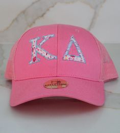 Bloom with pride in the Floral Appliqué Sorority Sister Cap! This lively pink trucker hat features beautiful, hand-appliquéd KΔ Greek letters in a charming floral pattern, adding a pop of personality and sisterhood spirit. With breathable mesh backing and an adjustable fit, it's the ultimate blend of style and comfort for sorority events, campus strolls, or everyday wear. Pink Baseball Cap With Letter Print, Pink Cotton Baseball Cap With Letter Print, Spring Embroidered Pink Baseball Cap, Embroidered Pink Baseball Cap, Pink Trucker Hat, Pink Baseball Cap With Embroidered Logo, One Size, Sorority Events, Sorority Sisters, Greek Letters