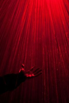 a person's hand reaching up into the air with red light shining on them