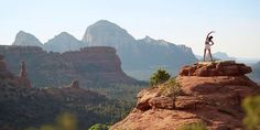 a person standing on top of a rock with their arms in the air and mountains in the background