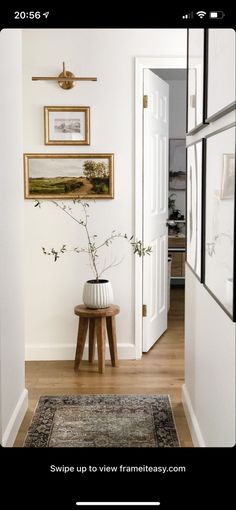 an entry way with pictures on the wall and a plant in a vase next to it