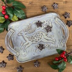 a decorative tray with holly and berries around it on a wooden table next to leaves