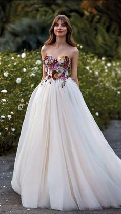 a woman in a white dress with flowers on the bouncy skirt is standing outside