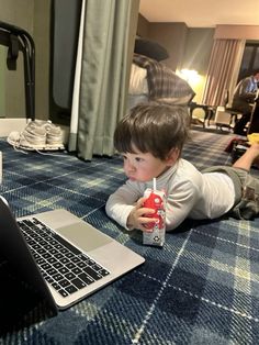 a young boy laying on the floor next to a laptop computer with a drink in front of him