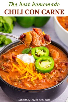 a spoon full of chili con carne with cheese and jalapenos in the background