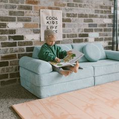 a little boy sitting on top of a blue couch next to a wooden coffee table