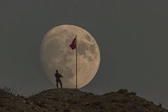 a man standing on top of a hill with a flag in front of the moon