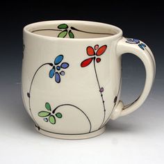 a white coffee cup with colorful flowers painted on the outside and inside, sitting on a gray surface