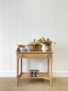 a wooden table topped with books and vases filled with orange flowers next to a white wall