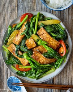 a white plate topped with tofu and veggies next to chopsticks