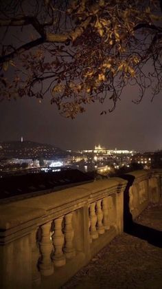 the city lights are lit up in the night sky from an old stone wall with railings