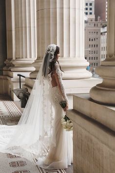 a woman in a wedding dress standing next to columns and looking down at the ground