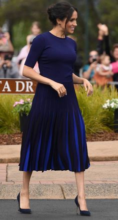 a woman in a blue dress is walking down the street with her hand on her hip