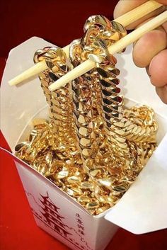 someone is holding chopsticks over some gold coins in a box that has been opened