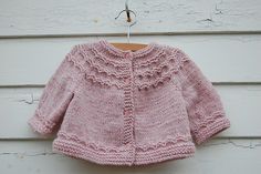 a pink knitted sweater hanging on a clothesline next to a white wooden wall