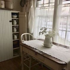 a white vase with flowers sitting on top of a wooden table next to a window