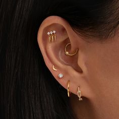 a woman wearing three different ear piercings on her left ear and the other two are gold