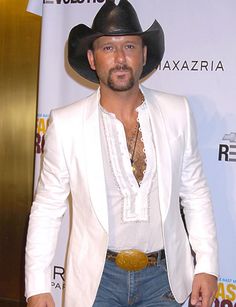 a man in a white suit and cowboy hat standing on the red carpet at an event