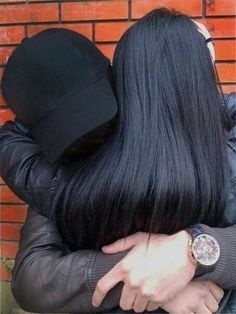 two people hugging each other in front of a brick wall with a watch on their wrist